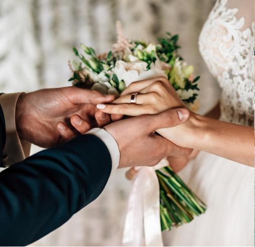 A bride holding a bouquet as the groom places a ring on her finger