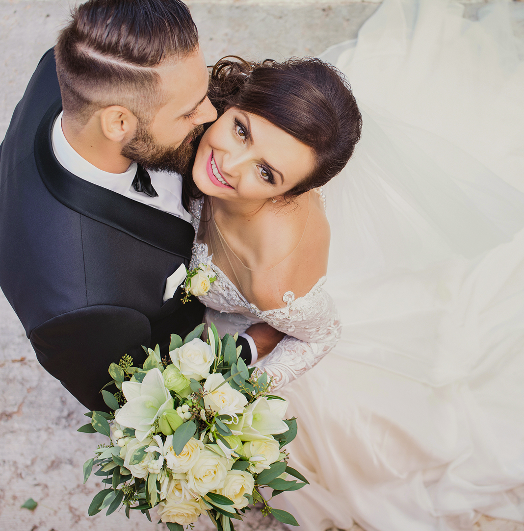 Bride and groom embracing on their wedding day, with the bride holding a bouquet of white flowers.