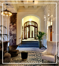 Elegant hotel hallway with seating, chandeliers, and patterned carpet.
