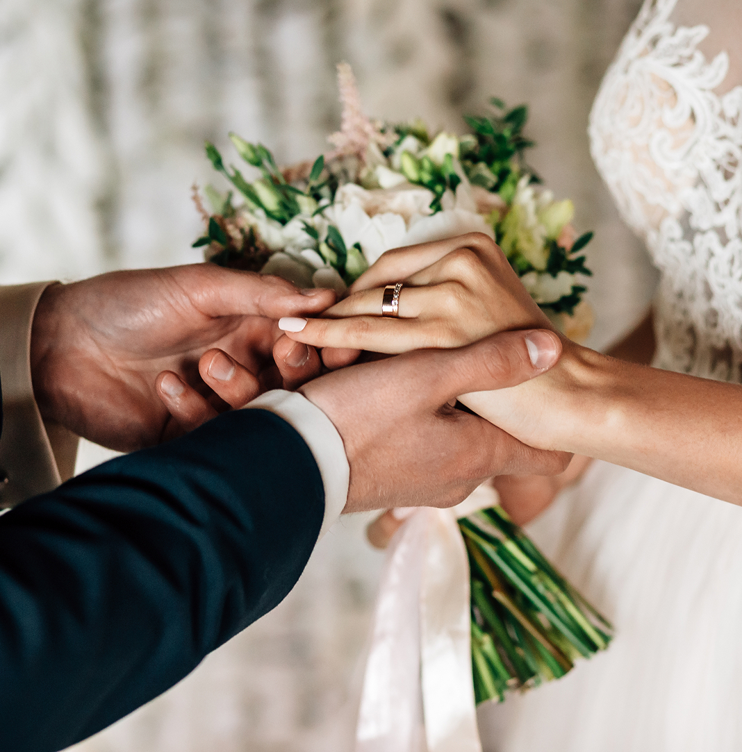Groom placing a ring on bride’s finger while she holds a bouquet