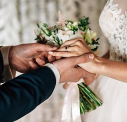 Groom placing a ring on bride’s finger while she holds a bouquet