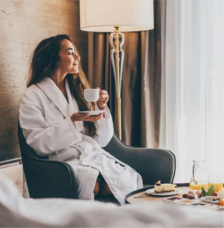 A woman in a bathrobe drinking coffee while sitting in an armchair