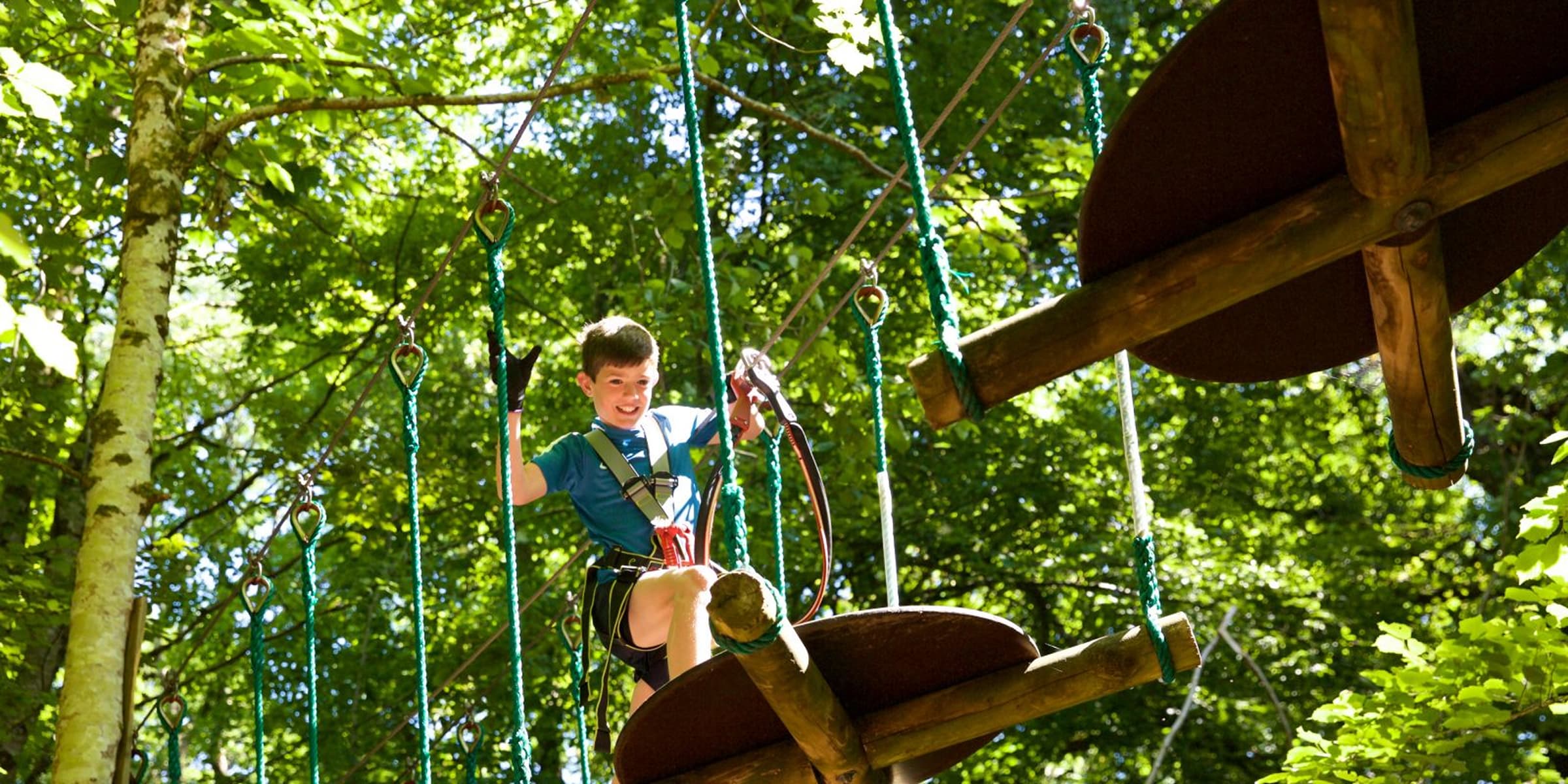 Smiling child enjoying an adventure ropes course among the trees.